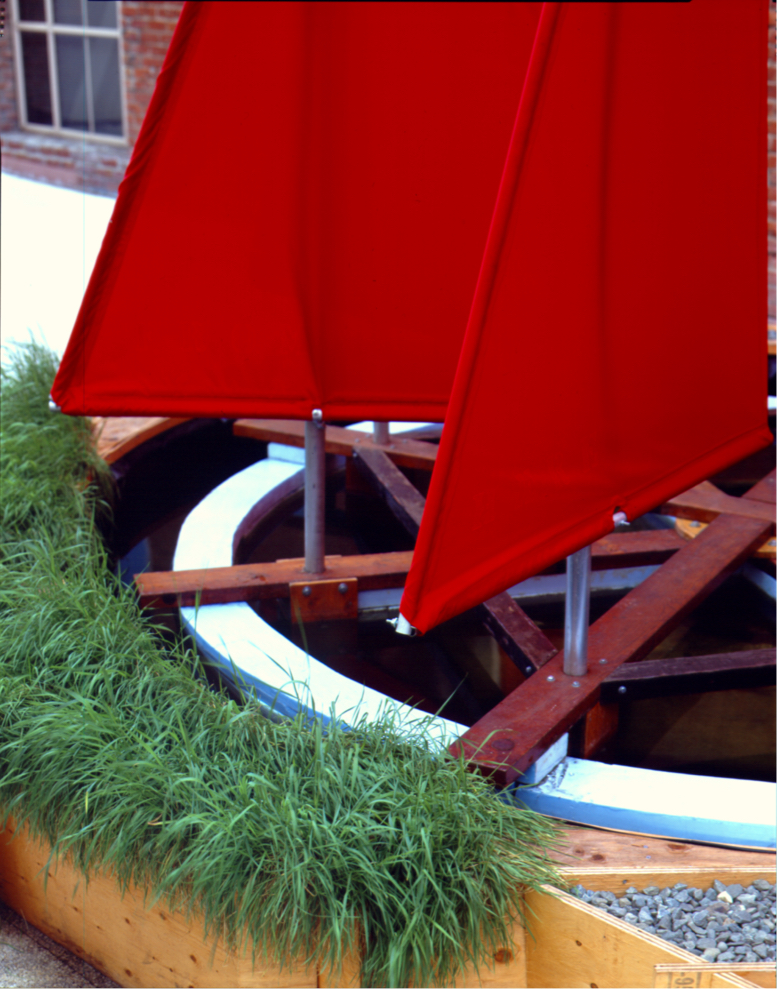 Detail: 2 sails mounted on ring, troughs filled with bushy grass and gravel.
