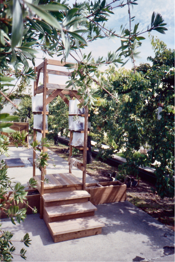 Tower on a cement walkway flanked by trees adjacent to buried journals.