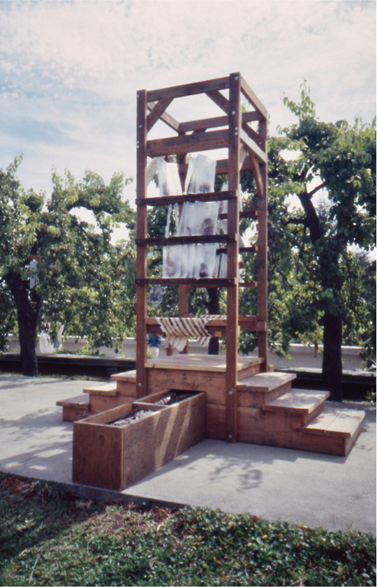 Wood tower with a center platform over a trough, accessed by 3 steps on each side.