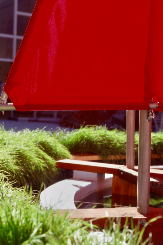Detail: sails mounted on ring flanked by grass growing alongside the pool's edge.