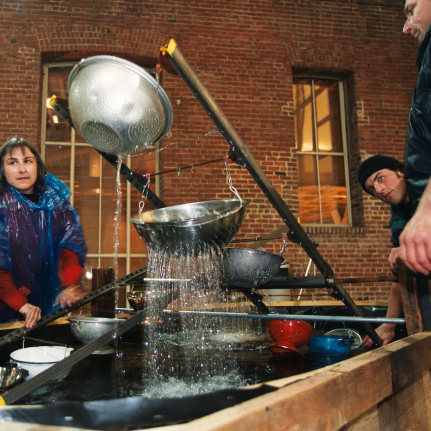 Water showers down when Judith, Darren, and Yari rock the colander see saw.