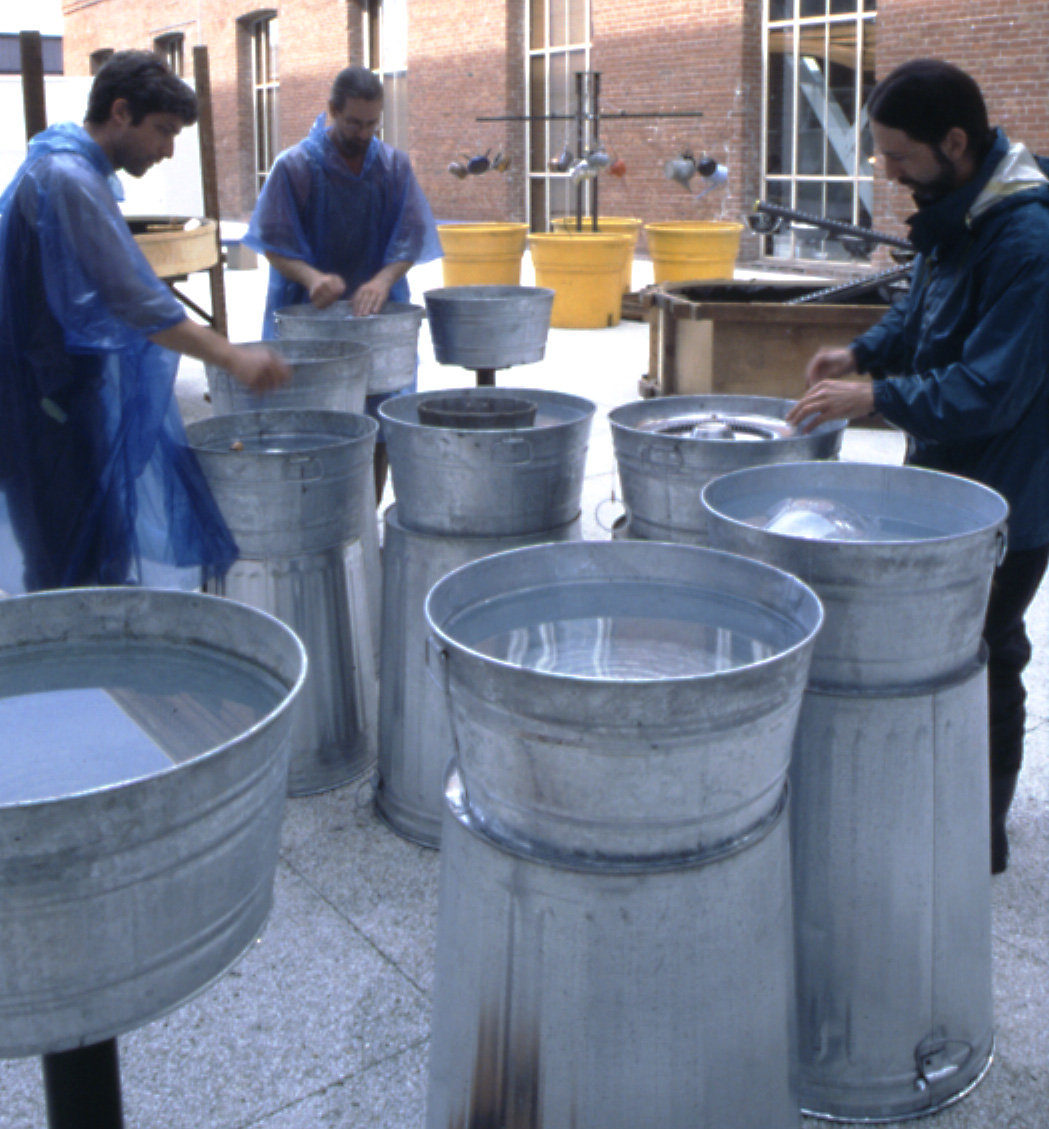 performers rehearse the metal water tubs sitting on top of metal garbage cans