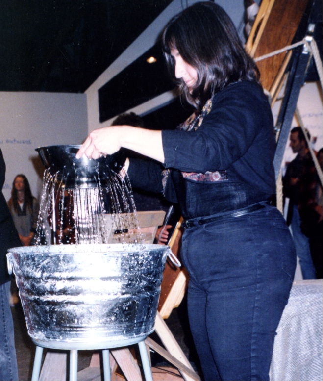 Judith holds a colander that is pouring water into a metal tub