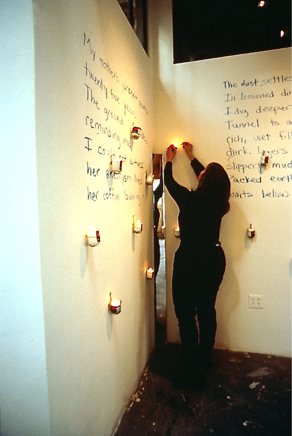 Judith lights a candle mounted to the wall which has a poem written on it.