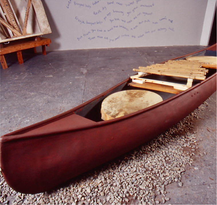 Canoe sitting on a bed of gravel, with a drum and bamboo marimba in it.