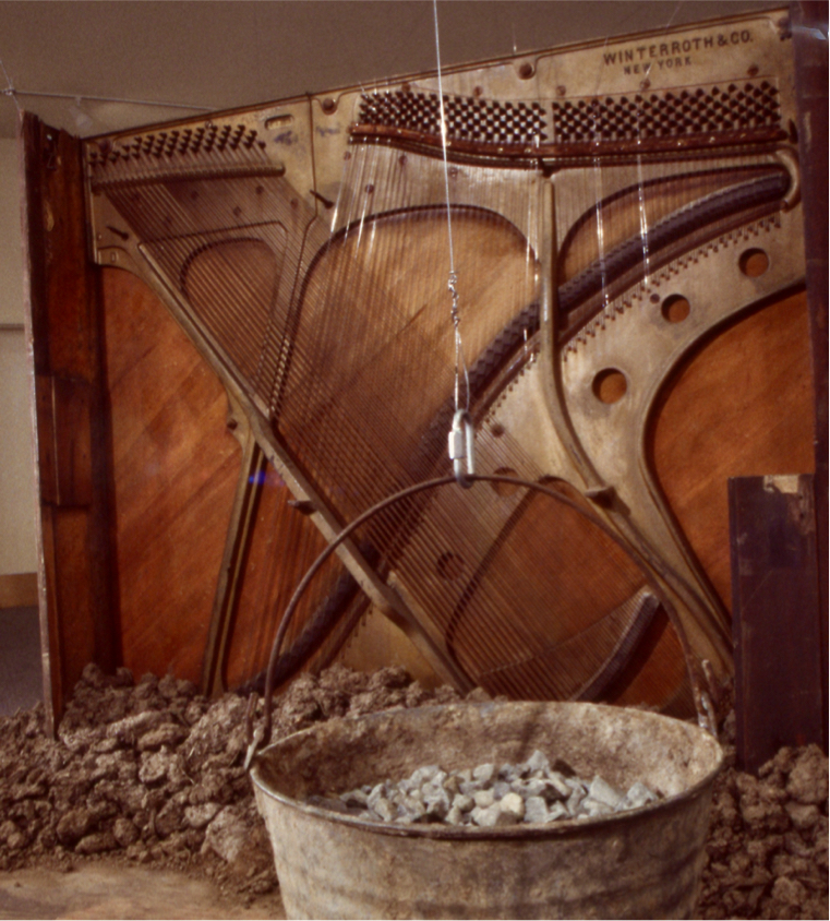 bucket of rocks in front of piano carcass showing the exposed stringed piano harp
