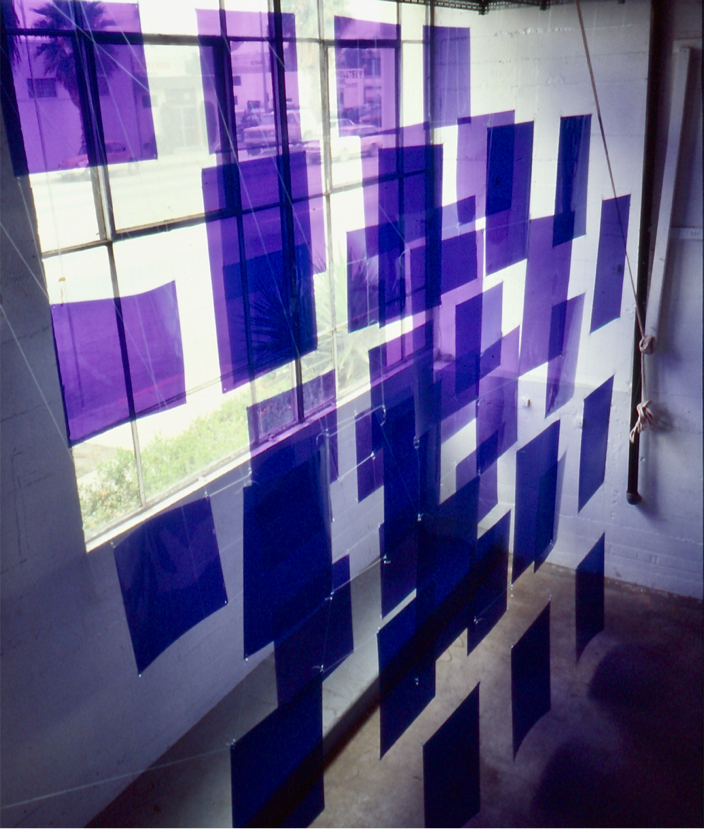 Sheets of translucent dark blue gels hang in rows in front of a large window.