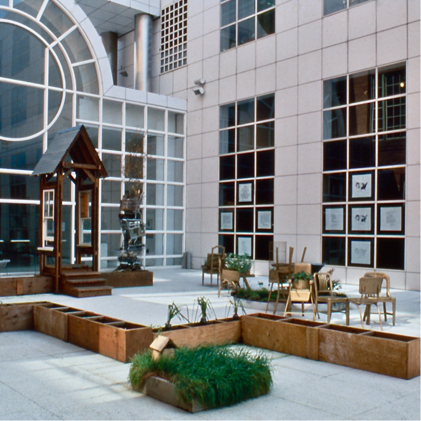 Installation shot with troughs, tower, snaking row of gold chairs in open air atrium.